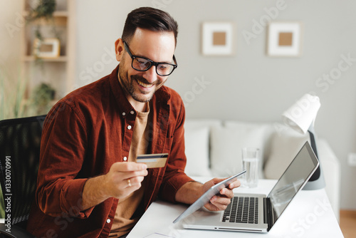 Happy male is making an online payment using his credit card and digital tablet