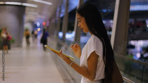 young asian woman on the big bridge touching the screen of her tablet standing in a white dress on the big avenue