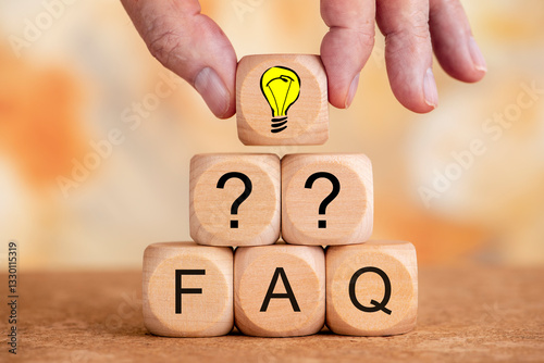 Obraz na płótnie Mehrere Holzwürfel bilden eine Pyramide und sind bedruckt mit Fragezeichen und FAQ, darüber eine Hand mit einem Holzwürfel bedruckt mit einem Glühbirne als Symbol für Idee oder Geistesblitz w salonie