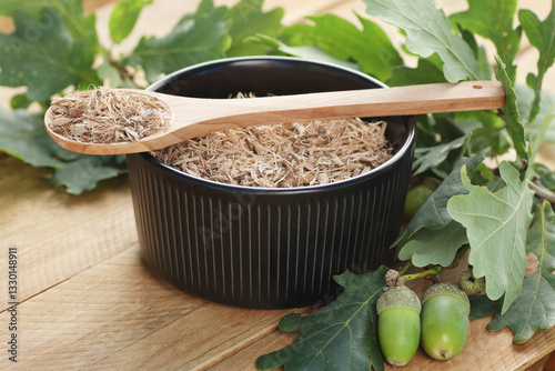 Oak bark in a bowl and spoon with leaves on wooden table, closeup, copy space, green medicine, healrhy drink for arthritis, diarrhea and bronchitis; for stimulating appetite; natural therapy concept photo