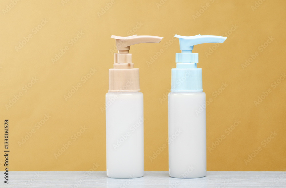 Two bottles of cream dispenser on the table, yellow background Two bottles of cream dispenser on the table, yellow background