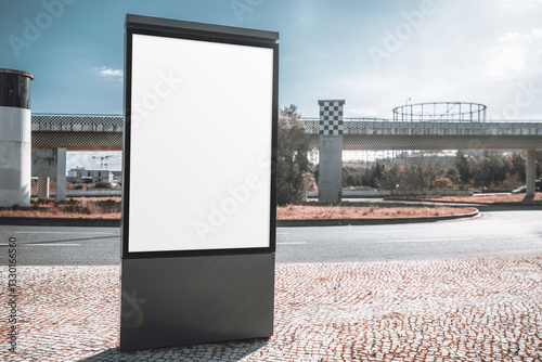 Wallpaper Mural Outdoor advertising mockup with a blank vertical billboard in an urban setting. The empty ad space stands on a cobblestone sidewalk near a road, with industrial structures in the background Torontodigital.ca