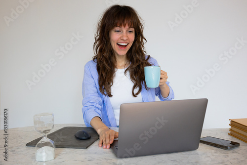 Surprised smiley curly brunette working at the laptop and drinking coffee got the message with good news