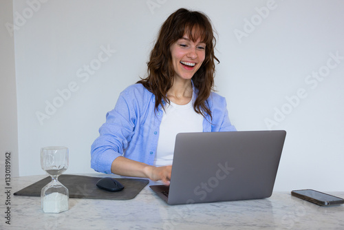 Beautiful smiley curly brunette sitting at the table with the laptop and typing with excitement