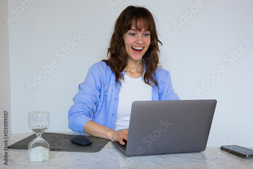 Beautiful smiley curly brunette sitting at the table with the laptop and typing with excitement