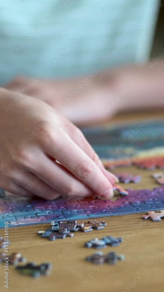 Close-up vertical view of young woman hands assembling puzzles at home. Connecting jigsaw puzzle pieces, assembling a jigsaw puzzle. Fun family leisure. Table games, home relaxation. Slow motion. Close-up vertical view of young woman hands assembling puzzles at home. Connecting jigsaw puzzle pieces, assembling a jigsaw puzzle. Fun family leisure. Table games, home relaxation. Slow motion.