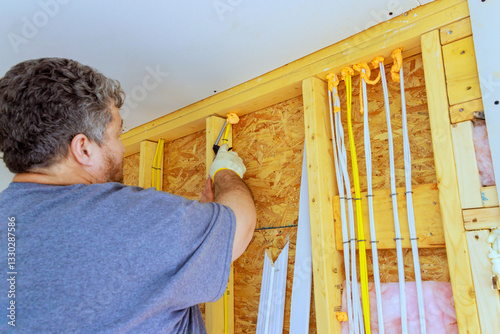 Worker uses spray can to apply foam insulation to wooden framing inside electrical components home during reconstruction