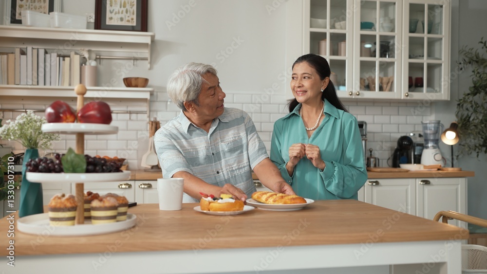 Smiling grandfather with casual cloth sitting at table while grandmother presenting breakfast. Senior couple talking and spending time or supporting together. Healthy relationship concept. Myrmidon. Smiling grandfather with casual cloth sitting at table while grandmother presenting breakfast. Senior couple talking and spending time or supporting together. Healthy relationship concept. Myrmidon.