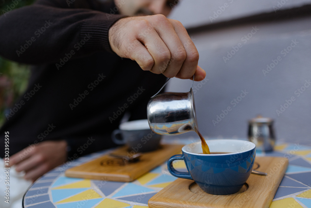 Pouring Rich Coffee Into a Vibrant Blue Cup at a Cozy Outdoor Cafe During a Sunny Afternoon Pouring Rich Coffee Into a Vibrant Blue Cup at a Cozy Outdoor Cafe During a Sunny Afternoon