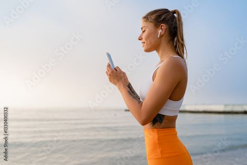pretty young smiling woman doing sports in the morning in stylish sport outfit sportswear, using smartphone