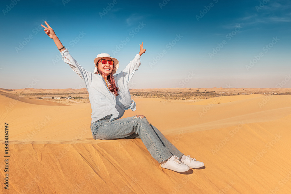 Carefree female tourist sitting on sand dune with arms raised enjoying desert landscape