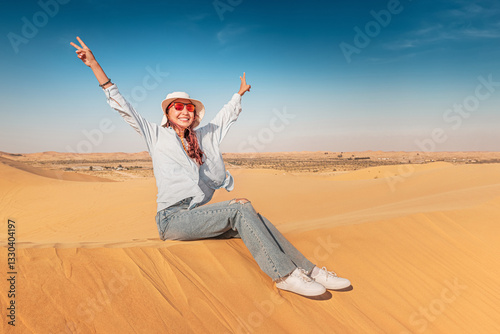 Obraz na płótnie Carefree female tourist sitting on sand dune with arms raised enjoying desert landscape w salonie