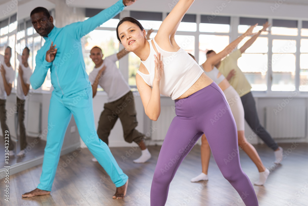 Asian girl teaches sequences of movements, actions during dance lesson, trains to doing hip hop dance, enjoys active hobby to music. Multinational group rehearsal, dance choreography coach Asian girl teaches sequences of movements, actions during dance lesson, trains to doing hip hop dance, enjoys active hobby to music. Multinational group rehearsal, dance choreography coach