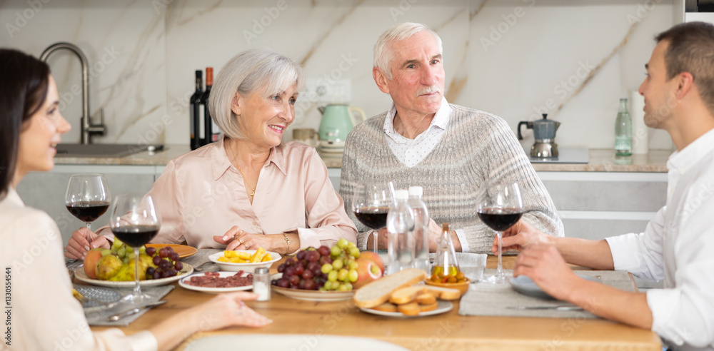 Mature spouses sitting at table, enjoying food and wine, chatting talking laughing with adult son and his girlfriend. In homely atmosphere male and female pensioner celebrate anniversary with guests Mature spouses sitting at table, enjoying food and wine, chatting talking laughing with adult son and his girlfriend. In homely atmosphere male and female pensioner celebrate anniversary with guests
