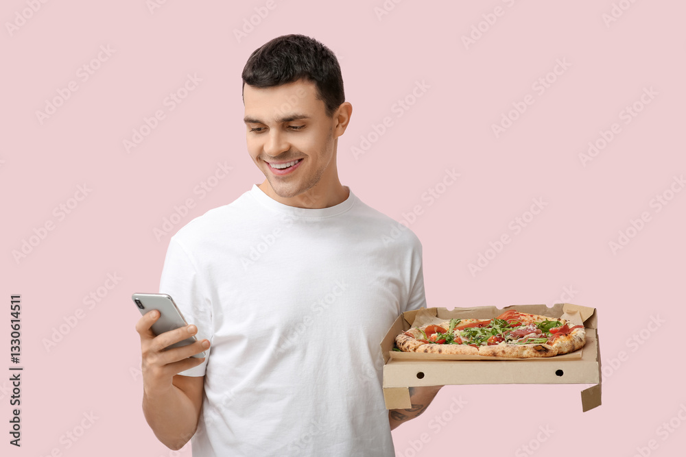 Young man holding cardboard box with tasty pizza and mobile phone on pink background Young man holding cardboard box with tasty pizza and mobile phone on pink background