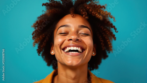 Closeup portrait of a young woman with curly hair laughing against a blue background. Ideal for advertising, social media, or articles about happiness.
