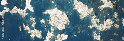 Peeling paint on the wall. Panorama of a concrete wall with old cracked flaking paint. Weathered rough painted surface with patterns of cracks and peeling. Panoramic texture for background and design.