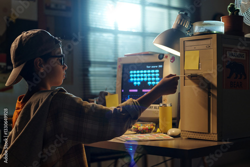 Foto Young kid using an old computer in a dimly lit room, wearing a cap and large gla