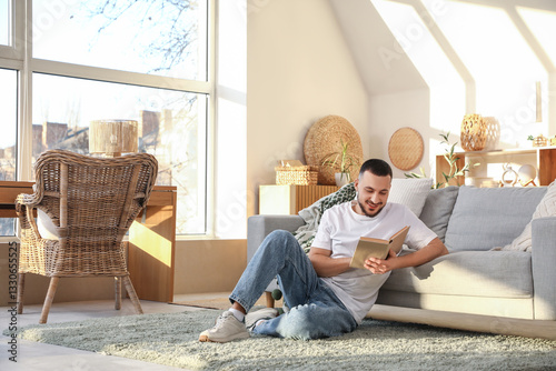 Handsome young man reading book on floor in stylish living room with big window photo