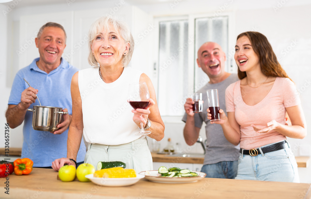 Happy family of four with glasses of wine in their hands is preparing a festive dinner in a home kitchen Happy family of four with glasses of wine in their hands is preparing a festive dinner in a home kitchen