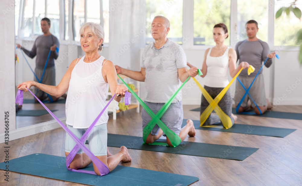Naklejka premium Elderly woman doing pilates exercises with elastic band in group in fitness studio
