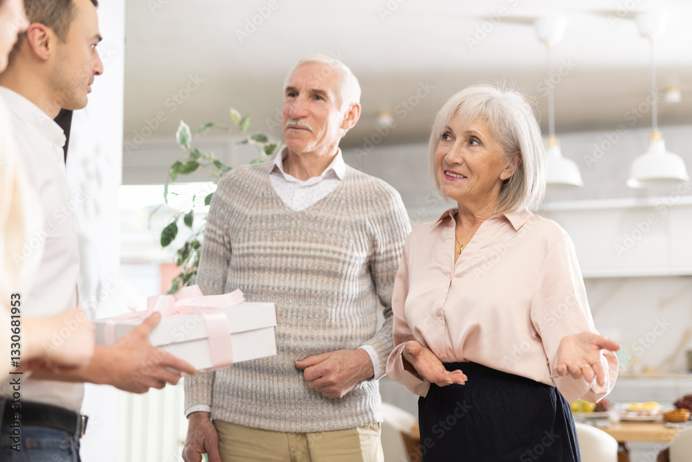 Obraz premium Happy senior man and woman welcoming young couple during small gathering with family members at home