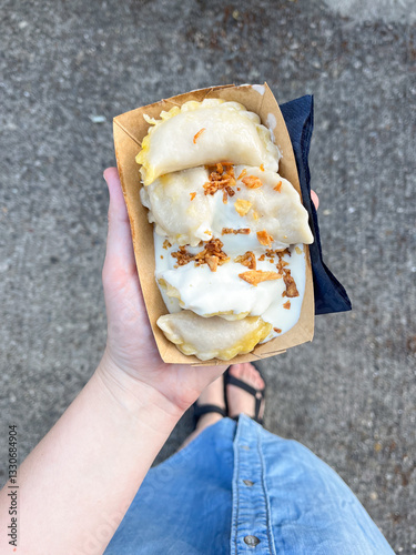 Top view of woman's hand holding a disposable plate with dumplings with sour cream and dried onion. Traditional Ukrainian Food. Street Food.