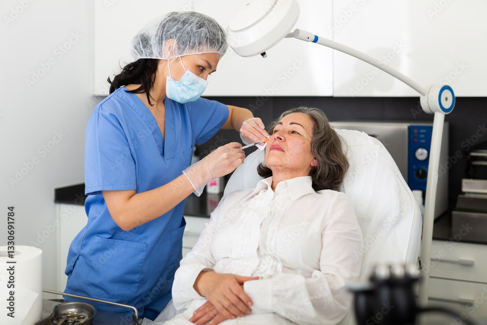 Obraz premium Qualified focused cosmetologist giving beauty injections for face skin rejuvenating and tightening for elderly female client in aesthetic medicine office