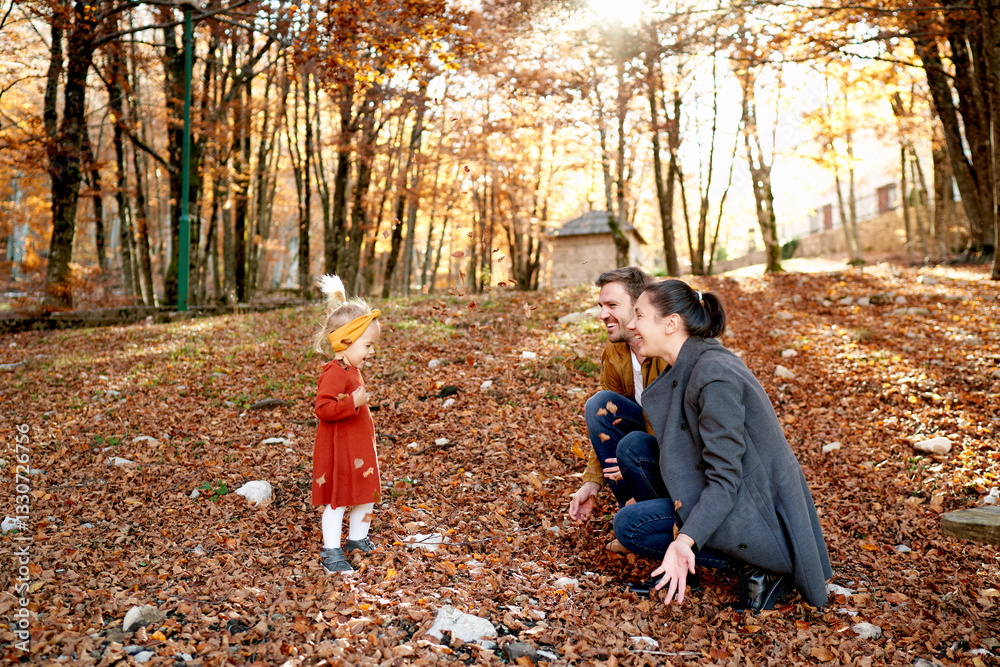 Fototapeta premium Little girl stands in front of smiling mom and dad squatting in the forest