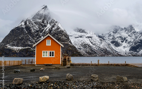 Traditional yellow rorbu house and Olstind mountain peak in Sakrisoy fishing village, Lofoten, Norway photo