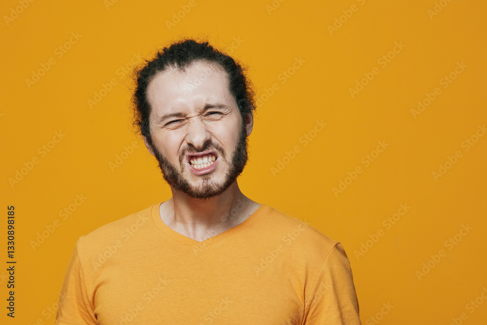 Young man with curly hair and beard expressing frustration against a bright yellow background, wearing a casual orange t shirt, ideal for illustrating emotions Young man with curly hair and beard expressing frustration against a bright yellow background, wearing a casual orange t shirt, ideal for illustrating emotions