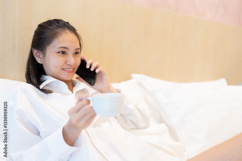 An Asian woman walks into her luxurious hotel bedroom, excited to relax on her vacation, talking on the phone and enjoying a delicious drink before heading out to the beach. An Asian woman walks into her luxurious hotel bedroom, excited to relax on her vacation, talking on the phone and enjoying a delicious drink before heading out to the beach.
