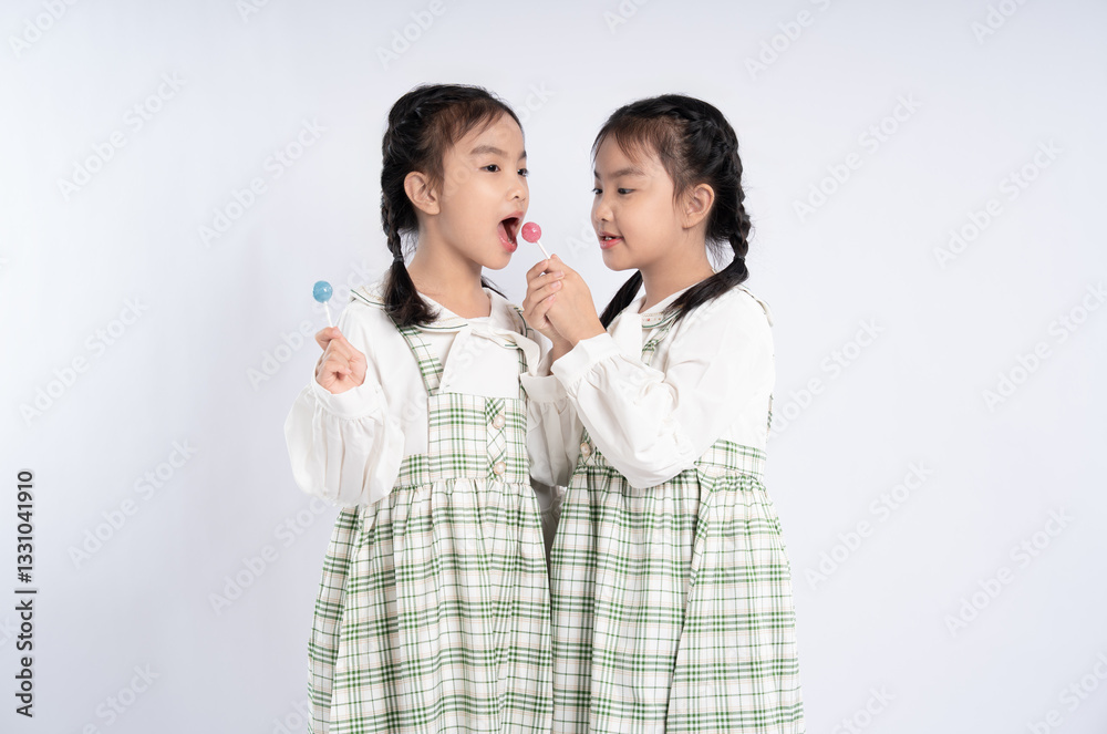 Twin girls sharing lollipops, dressed in matching plaid dresses, create a sweet and joyful moment together. Twin girls sharing lollipops, dressed in matching plaid dresses, create a sweet and joyful moment together.
