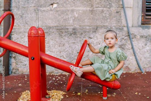 Little girl sitting on a swing balancer holding a handle on a playground