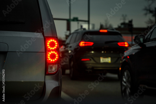 The red tail lights of a minivan turned on as the vehicle is stationary in traffic with other cars surrounding it.