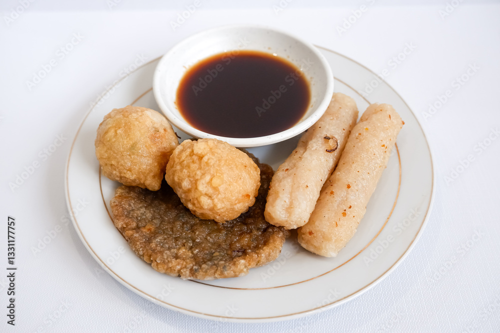 A plate of pempek (indonesian fish cake) with a variety of items including adaan (ball shaped), lenjer (long shape), and kulit (circle). The plate is set on a white background. A plate of pempek (indonesian fish cake) with a variety of items including adaan (ball shaped), lenjer (long shape), and kulit (circle). The plate is set on a white background.