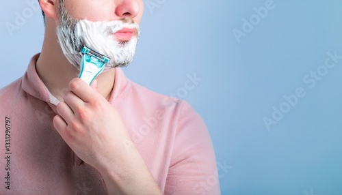 a man shaving his beard with a razor, focus on shaving foam and skin with blue background. the man is carefully using the razor photo