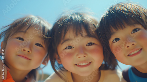 Obraz na płótnie 日本の小学生・幼稚園児・保育園児3人がカメラを覗き込んで笑っている写真 背景青空 w salonie