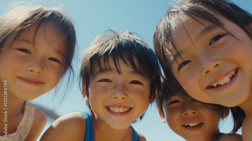 日本の小学生・幼稚園児・保育園児4人がカメラを覗き込んで笑っている写真 背景青空 夏