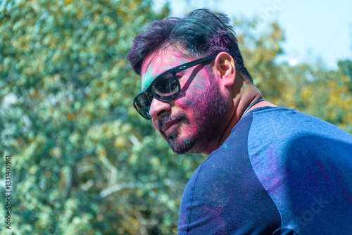 Happy young Indian man with colored face having fun playing with colorful powder color or gulal celebrating holi festival	