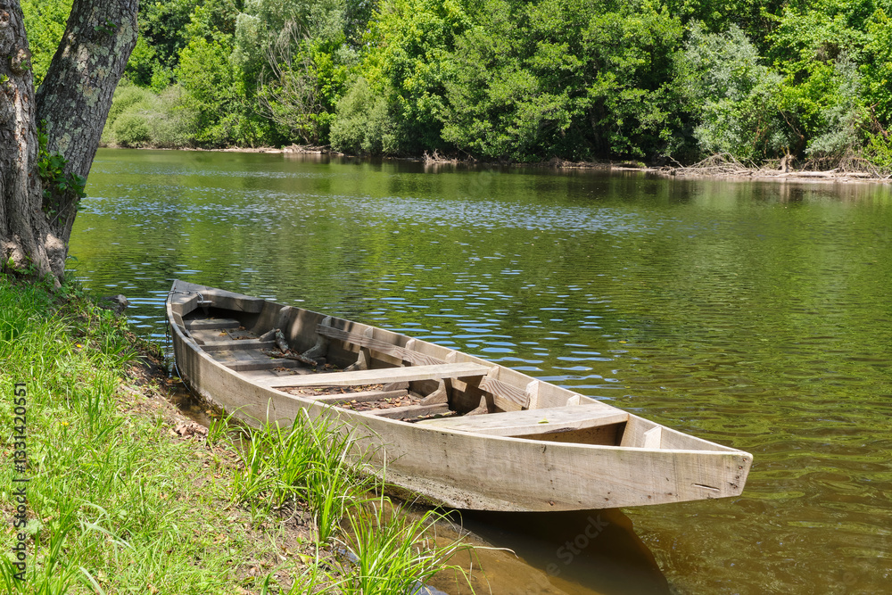 Small wooden unpainted boat in the Dordogne river near the village of Carennac in Lot Occitanie Southern France under a blue sky in summer.	