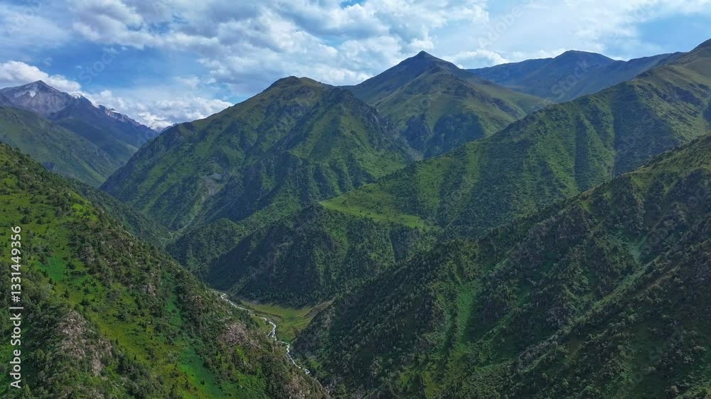 A drone hyperlapse video moves forward over Semonovskoye Gorge in Kyrgyzstan, capturing a mountain valley with a river, green slopes, peaks, and drifting clouds under a blue sky. A drone hyperlapse video moves forward over Semonovskoye Gorge in Kyrgyzstan, capturing a mountain valley with a river, green slopes, peaks, and drifting clouds under a blue sky.