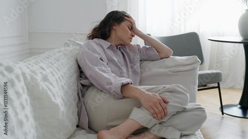 A young woman is suffering from a headache while sitting on the couch in the living room