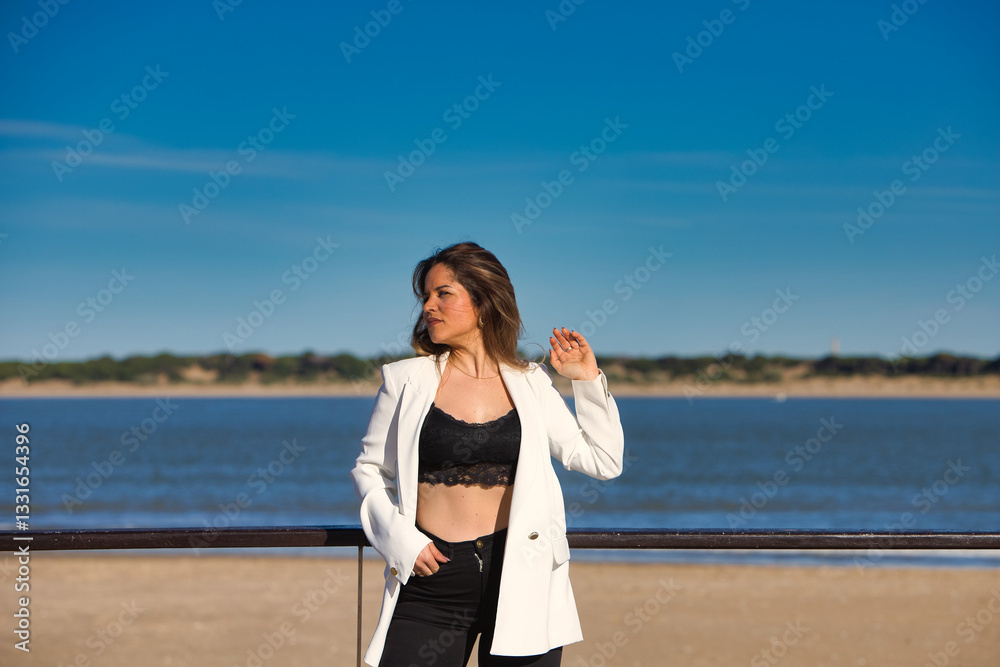 Young and beautiful blonde woman is leaning on the railing of the promenade at the mouth of the river, the woman looks to the side. In the background the blue sea. Young and beautiful blonde woman is leaning on the railing of the promenade at the mouth of the river, the woman looks to the side. In the background the blue sea.