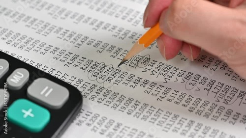Hand writing in a notebook with a pencil, calculator on desk