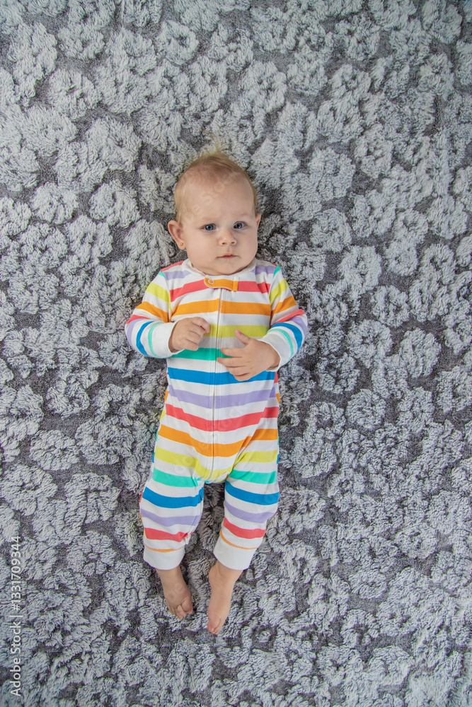 Fototapeta premium newborn baby girl playing with her feet, wearing a beautiful rainbow colored jumpsuit.