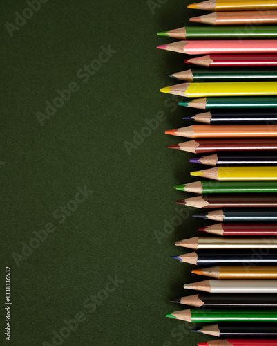 Wooden colored pencils scattered on a green school desk