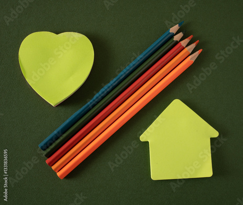Heart-shaped papers and houses on a school desk with colorful wooden pencils waiting for the teacher to write on them