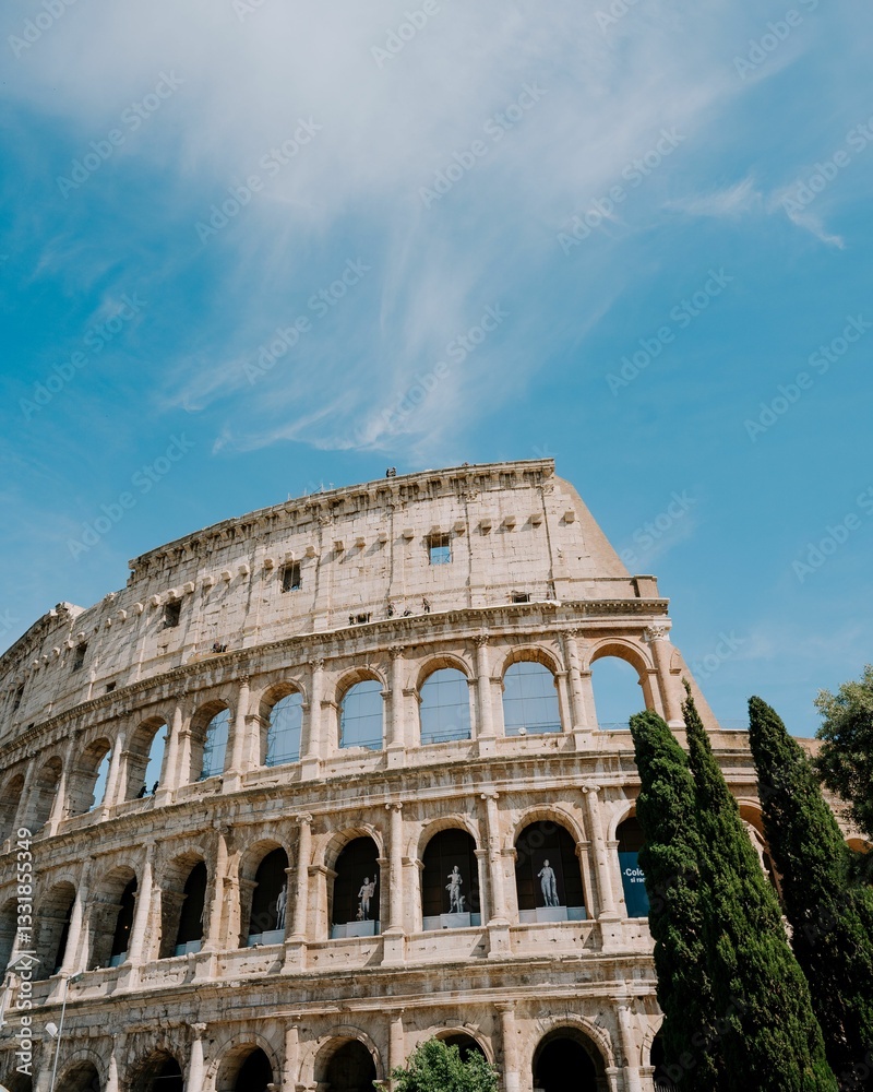 Fototapeta premium Colosseum in Rome with a clear blue sky and lush greenery in the foreground.