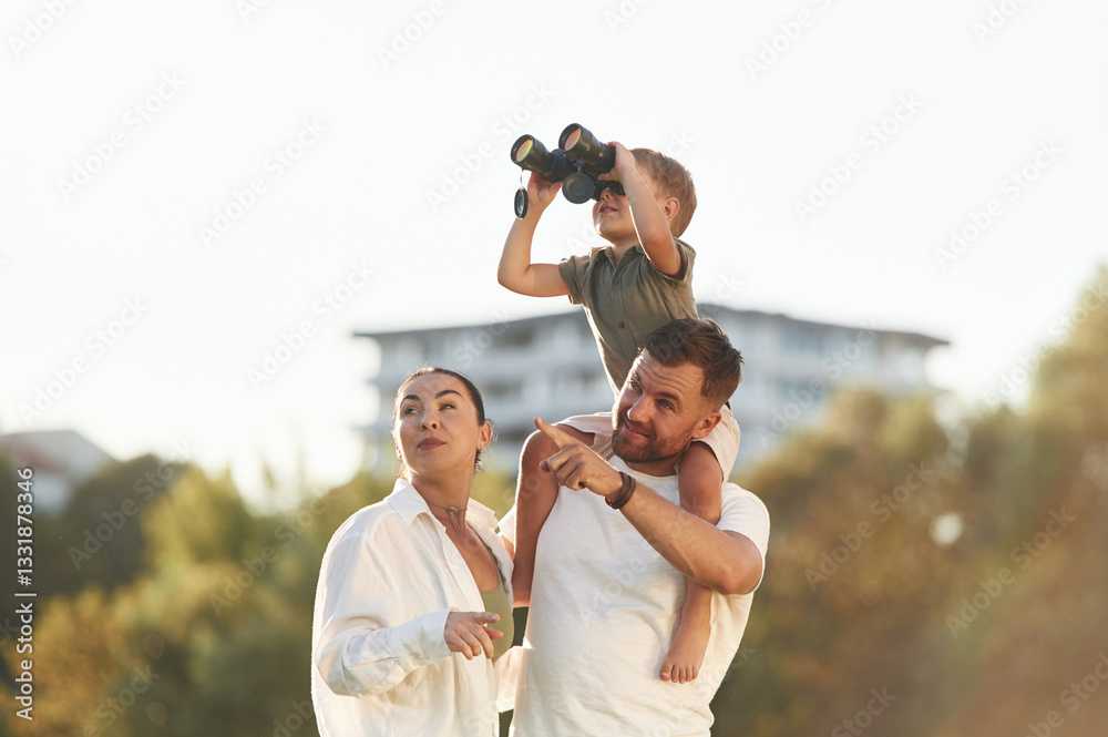 Black binocular in hands. Mother and father are with son outdoors on the field Black binocular in hands. Mother and father are with son outdoors on the field